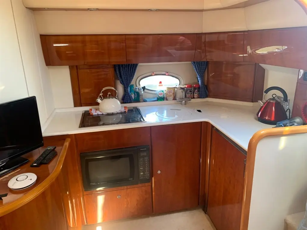 Compact boat kitchen featuring a microwave, stove, kettle, sink, and storage with a TV in a wood finish.